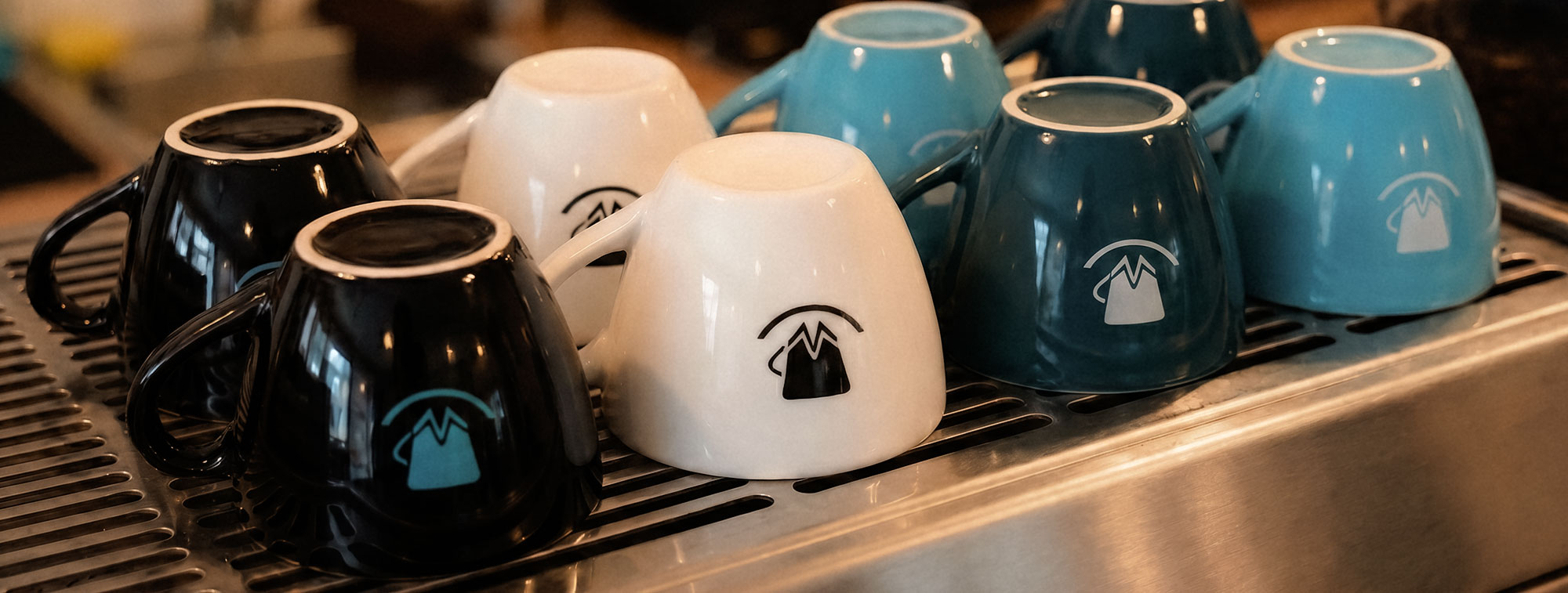 Ice Noir Cafe branded ceramic cups drying upside down on a professional espresso machine rack