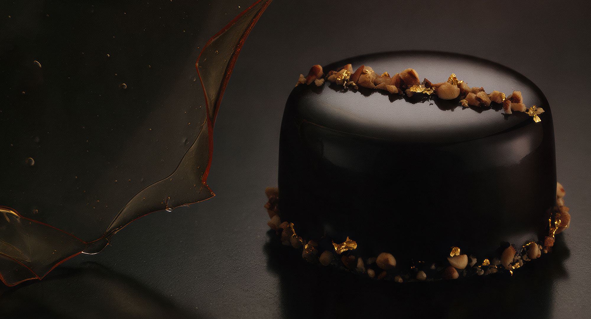 Chocolate and hazelnut pastry with a sculptural amber sugar ribbon on a dark background.
